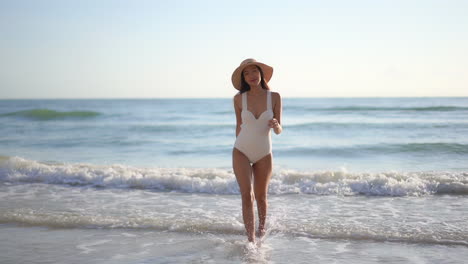 Asiatische-Sexy-Frau-Mit-Hut-Und-In-Einem-Weißen-Einteiligen-Badeanzug-Kommt-Selbstbewusst-Aus-Dem-Meer-Am-Strand