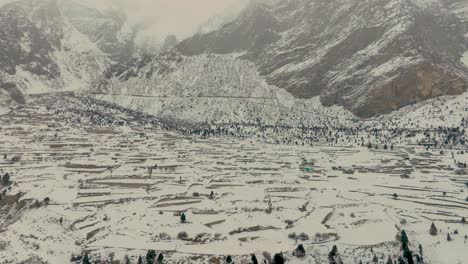 aerial view of snow covered rural village farmland in naltar valley floor, gilgit