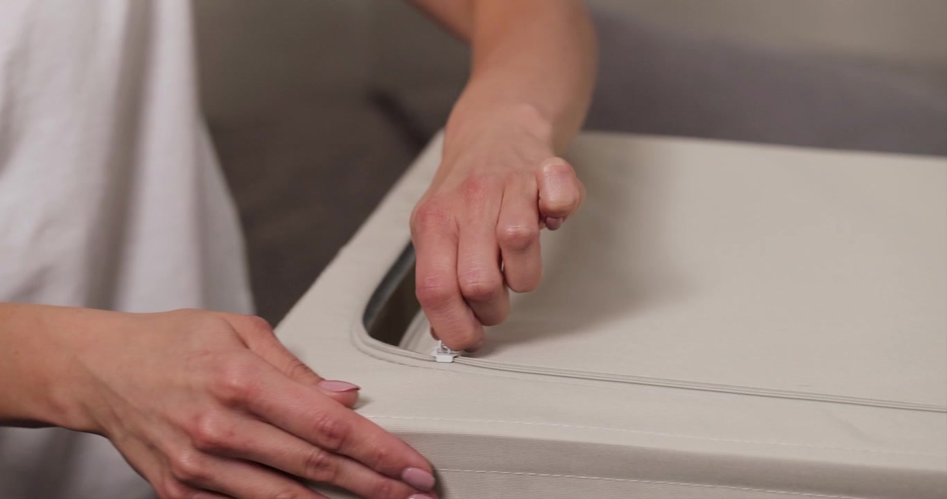 A close-up of a Caucasian woman’s hand with painted nails closing a clothing storage organizer, 4K resolution