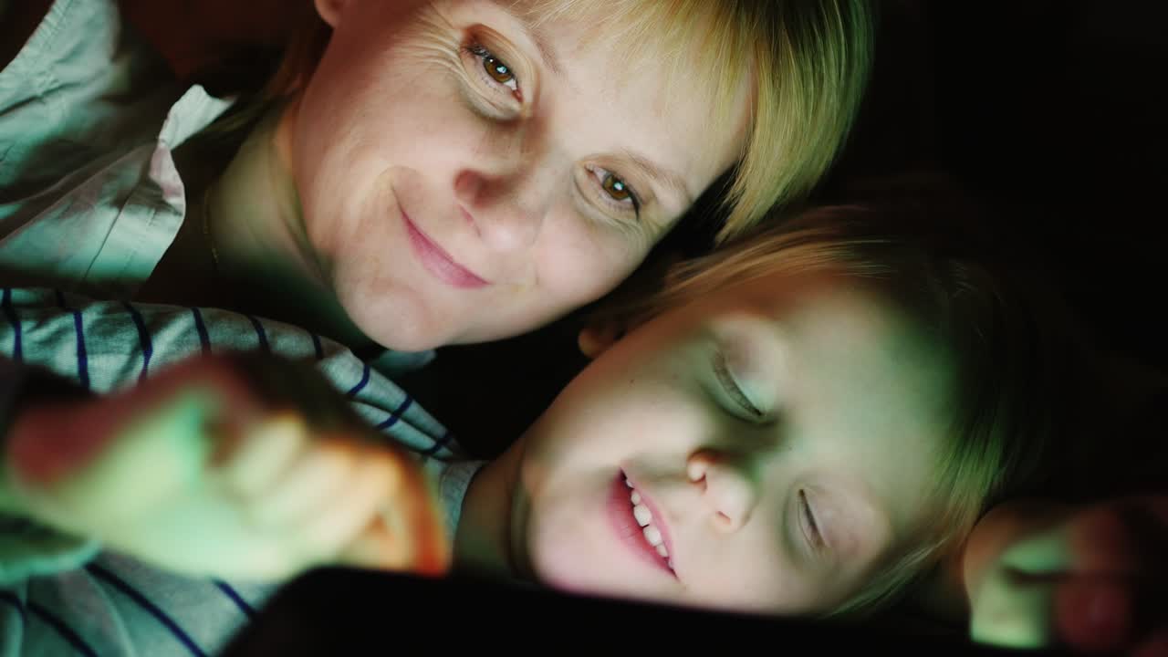feliz madre con su hija juntos juego en la tableta mentira uno al lado del otro cara a cara en la cama