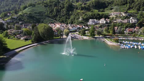 drone footage circling a large water fountain near a small town in the mountains