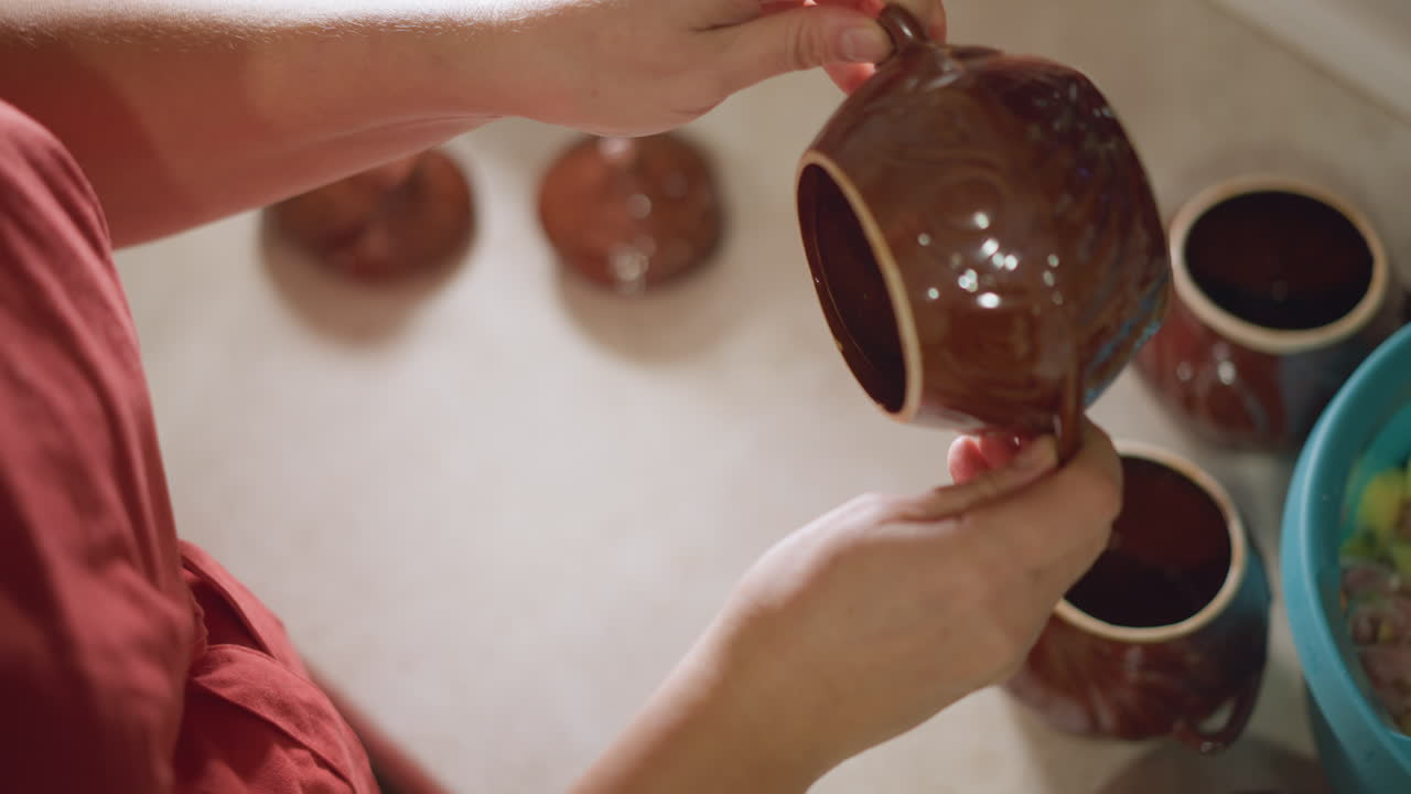 Mani esaminano ceramica. Primo piano di mani che ispezionano e ruotano ceramica in un ambiente cucina caldo. Vista dettagliata di mani che esaminano delicatamente e girano un vaso di argilla sotto una morbida illuminazione da cucina