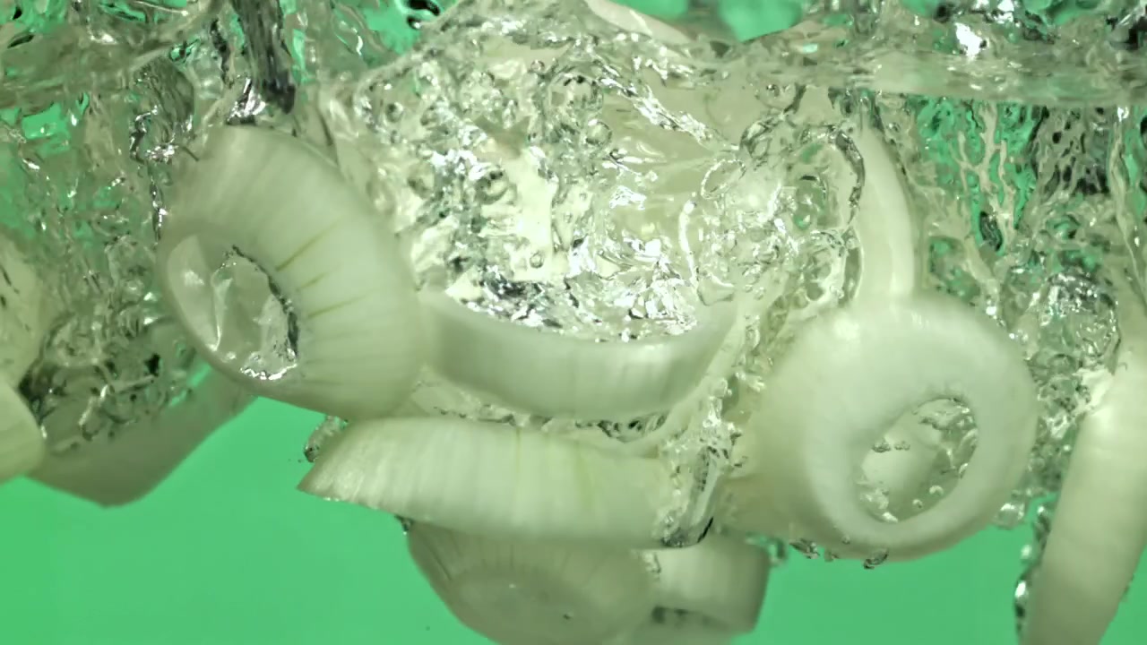 Slowmotion af friske løgringe, der falder ned i vand
