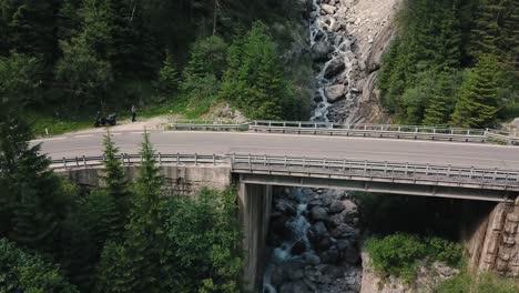 Crane-down-tilt-up-drone-shot-of-a-man-controlling-a-drone-and-a-bridge-over-a-river