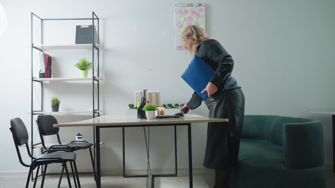 Businesswoman enters modern office, walks toward desk, places coffee cup and folder on surface, preparing to begin work in stylish and organized environment with office supplies and decorative plants