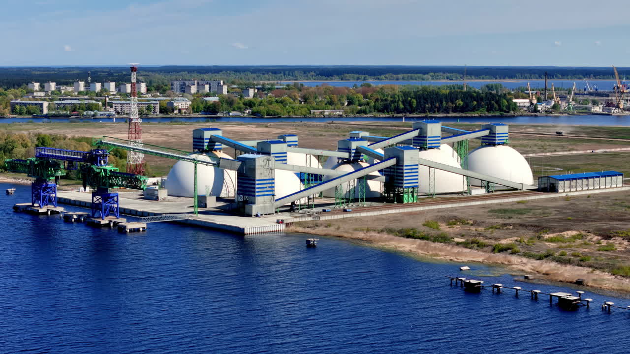 Panoramic Aerial View of a Modern Industrial Port Facility Specializing in Bulk Materials, Featuring Large White Storage Domes, Conveyor Belts, and Loading Piers on a Wide River or Estuary