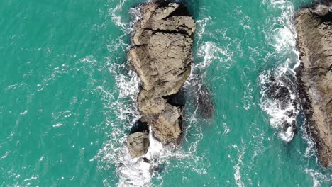 Drone-looking-down-flies-over-sea-stacks-in-teal-water