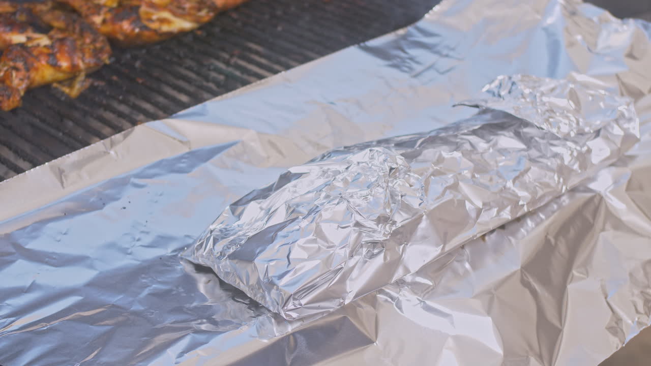 hombre con guantes de horno mueve las costillas envueltas en papel de aluminio a más papel de aluminio