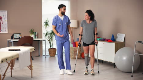 doctor talking to patient with prosthetic leg on crutches during physical therapy session