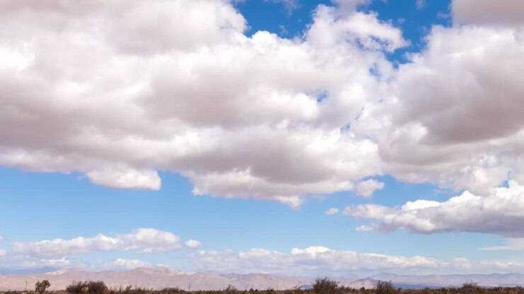 Il sole filtra tra gruppi di nuvole che attraversano il cielo sopra il paesaggio del deserto del Mojave - time lapse panoramico
