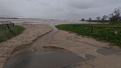 muddy spumes with water flowing on coastline with overcast. cyclone alfred at currumbin beach in queensland, australia. panning shot
