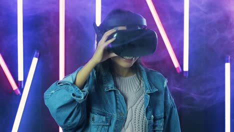 young woman looks around and wonders how amazing in the virtual reality. virtual reality helmet on color lighting smoke background