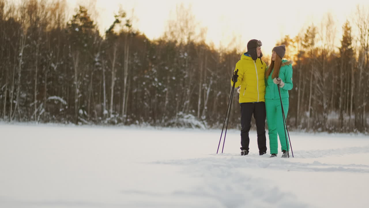en el bosque invernal al atardecer, un hombre y una mujer esquían y contemplan la belleza de la naturaleza y las atracciones en cámara lenta.