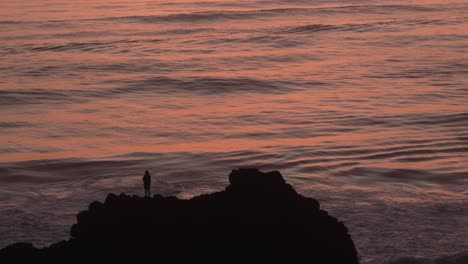 person standing on rock at the coastline of coolangatta silhouette shot during sunrise, orange reflection waves.