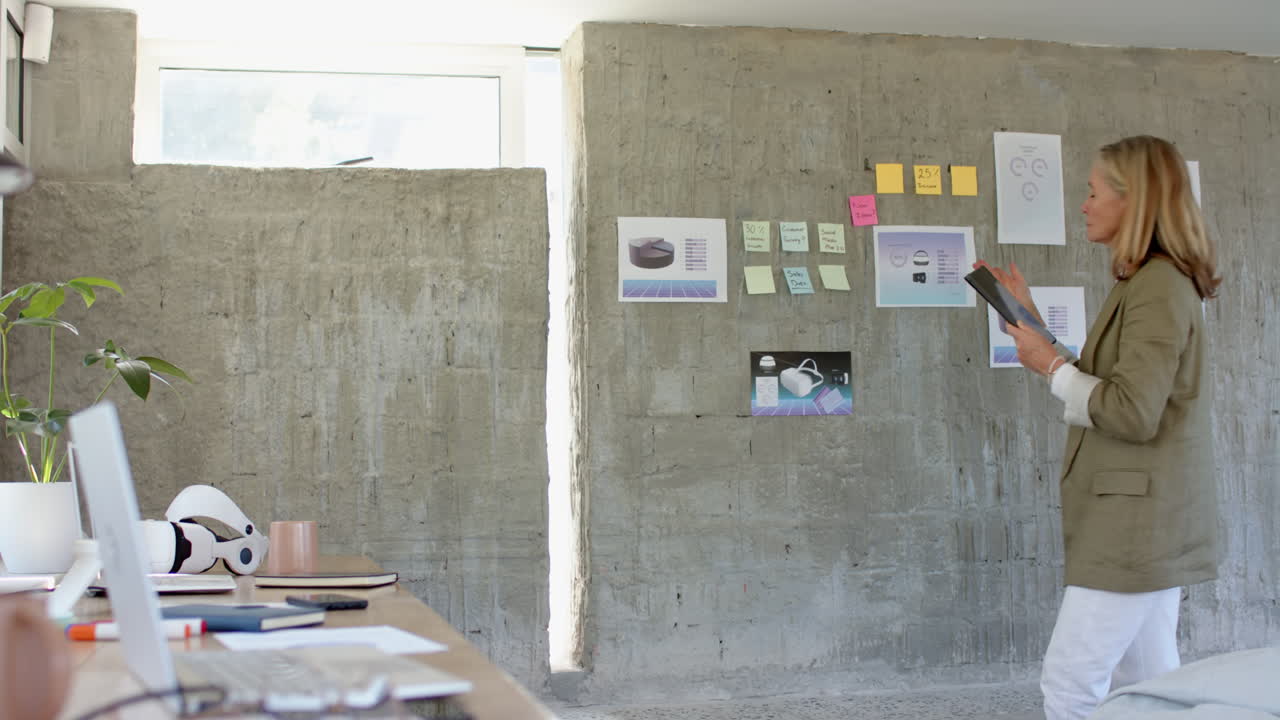 Using tablet, senior woman working in modern office with desk and documents