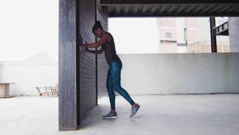 african american woman stretching leaning on a wall in an empty urban building