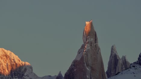 el icónico pico del cerro torre brilla con la cálida luz del amanecer contra un cielo despejado en la patagonia