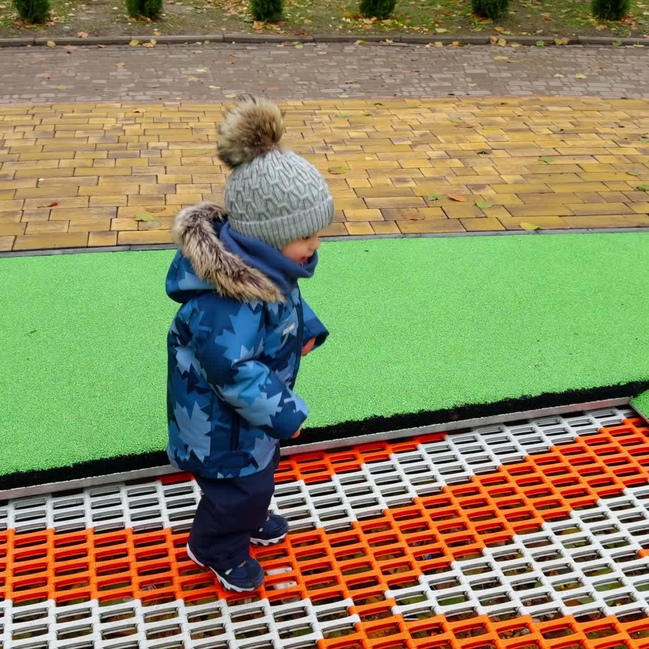 Bambino felice che indossa una giacca calda, un cappello e dei pantaloni mentre salta sul tappeto elastico. Bambino felice che trascorre del tempo all'aria aperta nel parco giochi in autunno