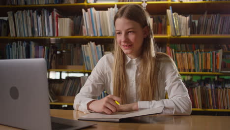 teen girl on online tutoring in the school library, using a laptop, handheld