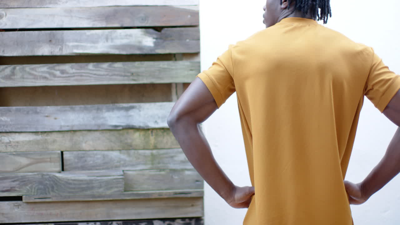 Rear view of african american man in yellow t shirt, with hands on hips, slow motion, copy space