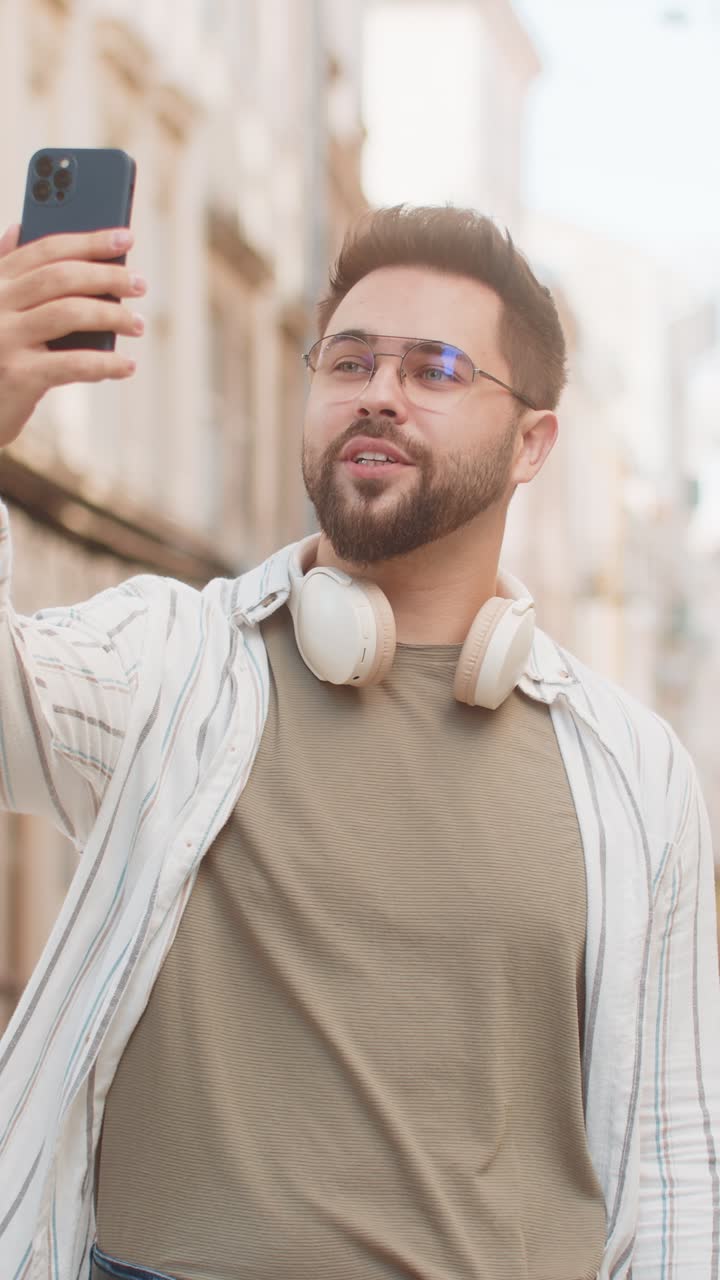 Giovane blogger caucasico che si fa un selfie sullo smartphone e fa una videochiama online in una strada della città