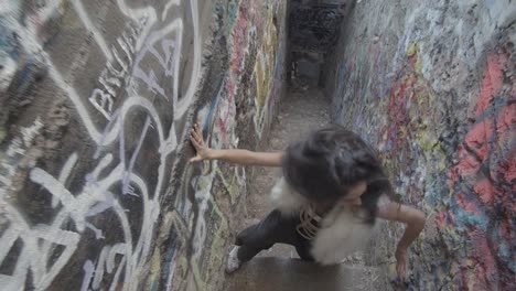 a young woman with a confused expression stumbles on the stairs of a narrow corridor covered with graffiti