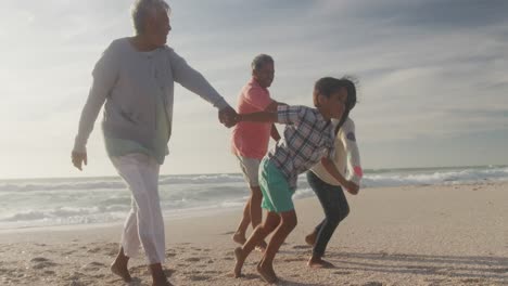 happy hispanic grandparents and grandchildren running on beach at sunset