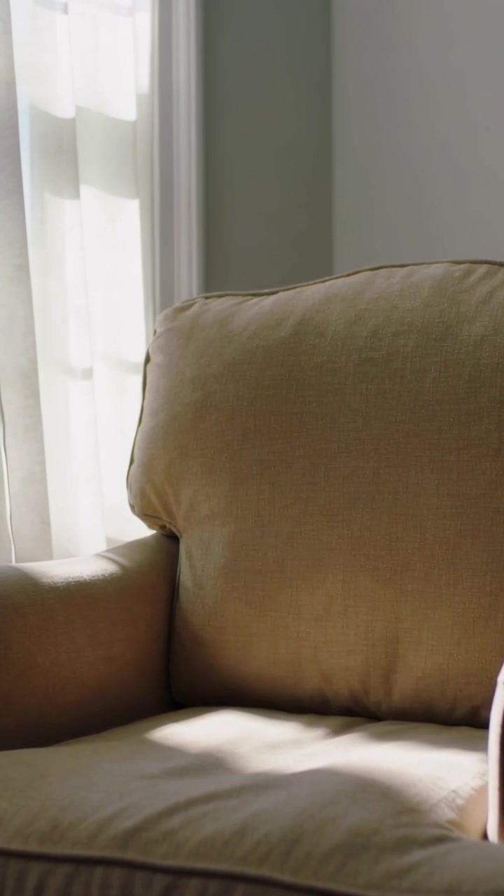Vertical video: Shifting sunlight shading beige armchair at tall window, revealing fur patch