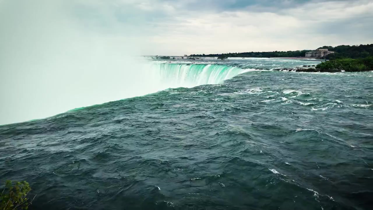 Szerokie zbliżenie turkusowej rzeki Niagara wpadającej do Wodospadu Horseshoe w Ontario, Kanada, z gęstą mgłą unoszącą się z ikonicznego wodospadu pod dramatycznym, zachmurzonym niebem.