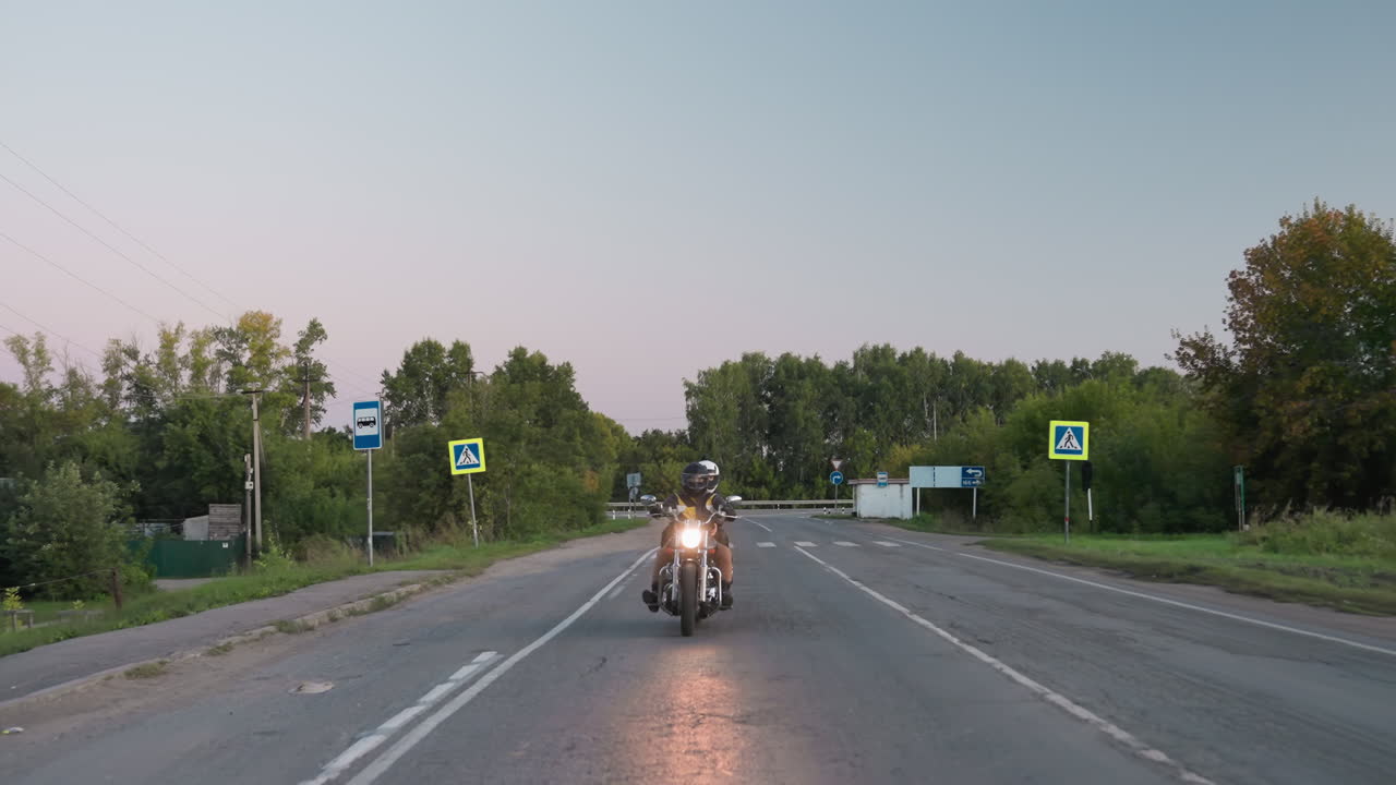 Family riding motorbike on road trip passes pedestrian crossing sign while car drives on opposite lane, evening sky over countryside trees and asphalt road