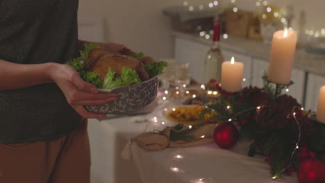 unrecognizable woman putting roast chicken on christmas dinner table