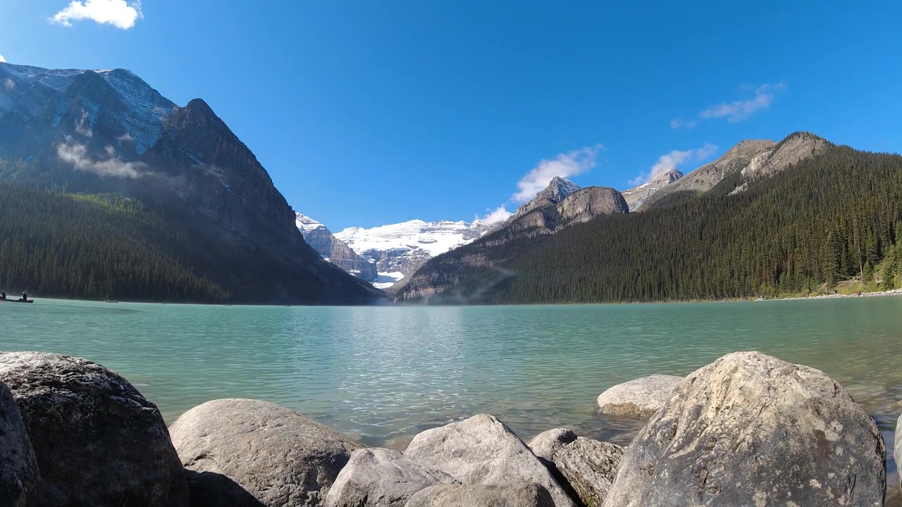 Nuvole basse si allontanano per rivelare un lago alpino turchese incorniciato da cime boscose e ghiacciai distanti in timelapse.