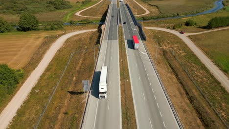 trucks driving on the highway through rural forested landscape, aerial view