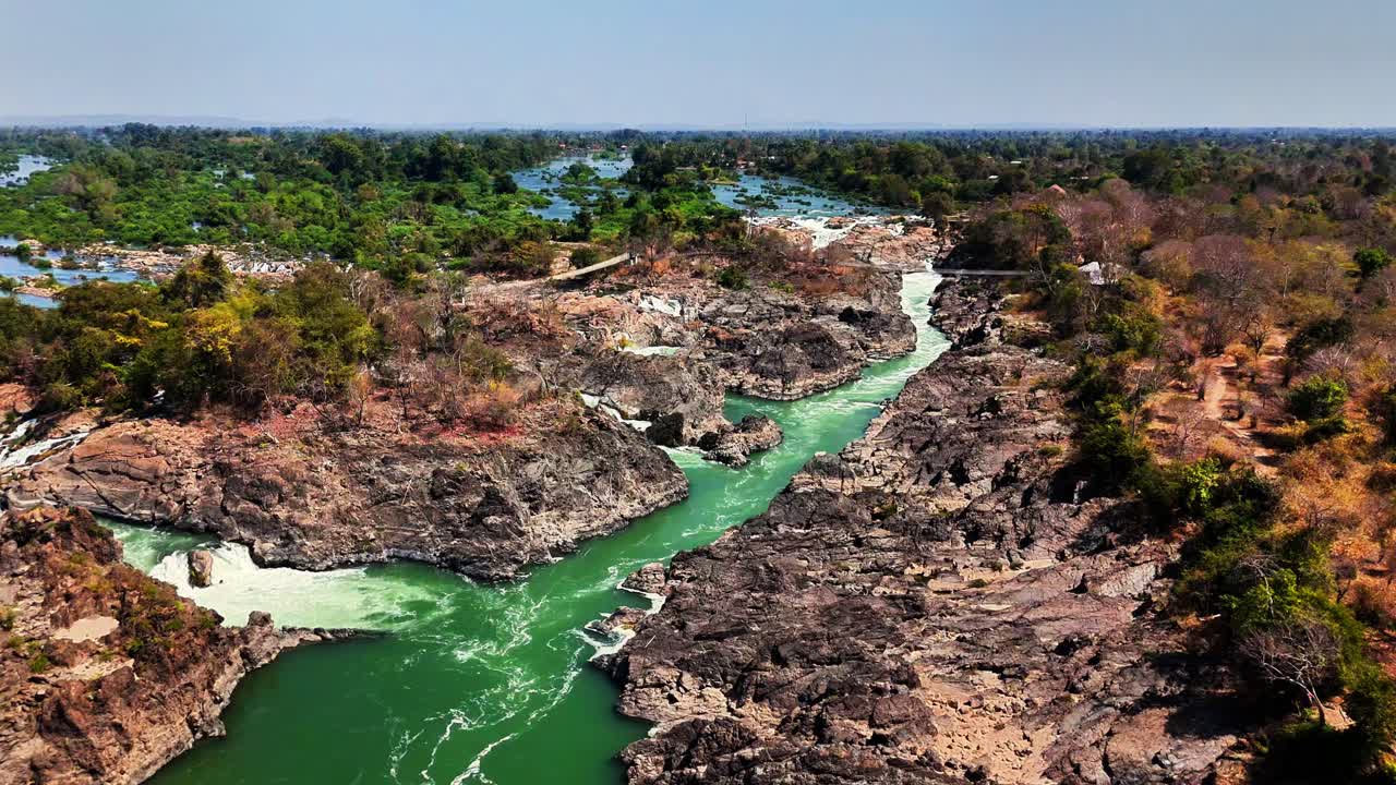 Drone view of the Mekong River carving through basaltic bedrock in Don Det, Laos, showing multiple waterfalls, steep rocky channels, and surrounding tropical floodplain forest
