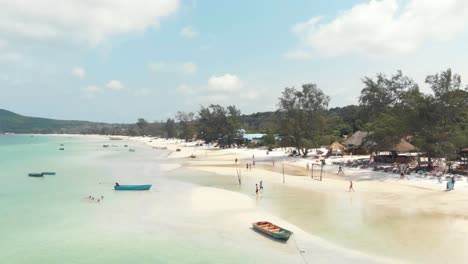 populated shallow exotic shore with tourists and fishing boats in saracen bay in koh rong sanloem, cambodia - aerial low angle fly-over shot