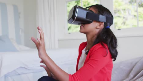 Mixed-race-girl-sitting-at-home-on-sofa-playing-wearing-virtual-reality-glasses
