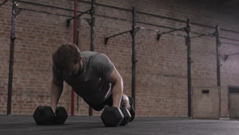 athletic man doing push ups on dumbbells