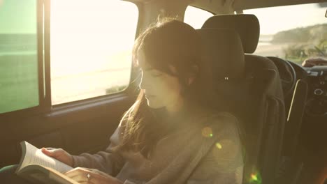 Mujer-Viajera-Leyendo-Un-Libro-En-Una-Camioneta-Al-Atardecer