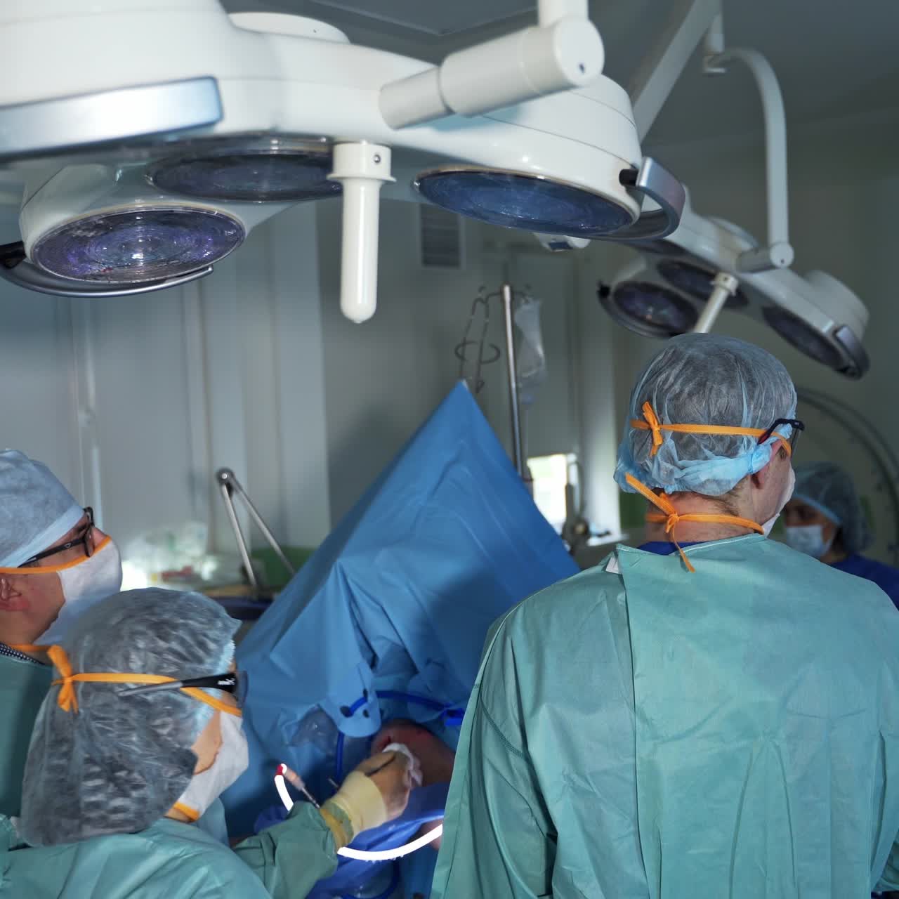 Chief surgeon turns the instrument in the cut of patient's body. Medical team follows the operation process on the screen