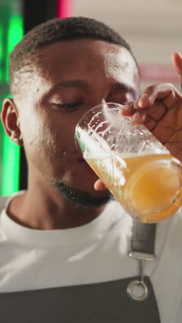 el barman bebe cerveza fresca en un pub de primer plano. el afroamericano toma un sorbo de una bebida alcohólica ligera y asente con la cabeza disfrutando de una calidad perfecta en el bar. el barman en el descanso