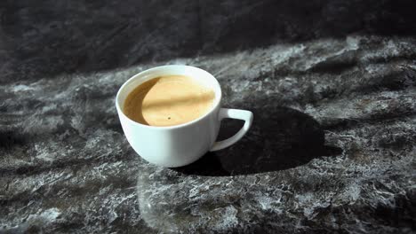 white cup containing coffee on a black and white mottled table