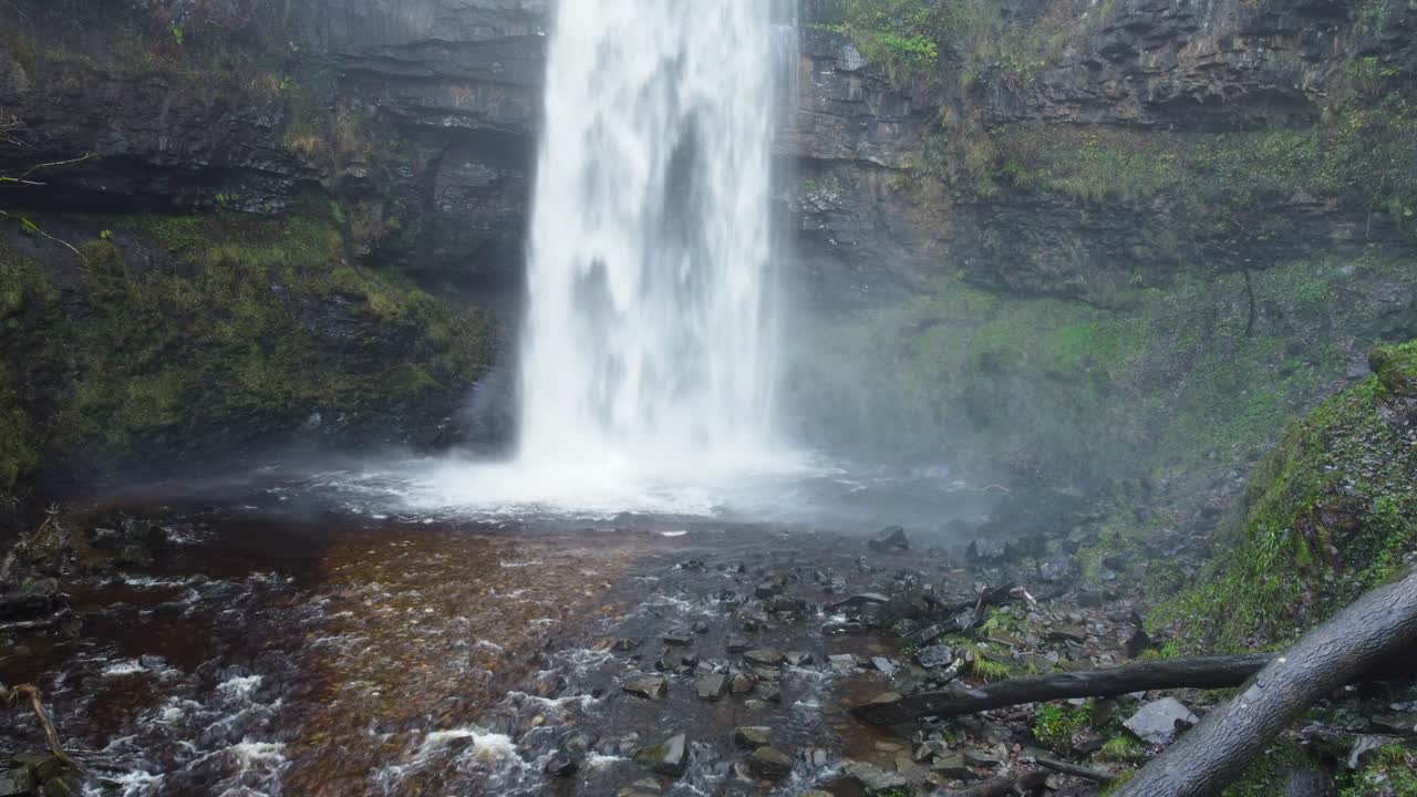 dron aéreo en cascada con cueva detrás y acantilado cubierto de musgo en gales, reino unido 4k
