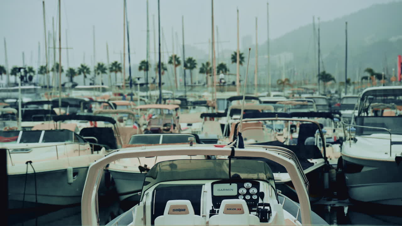 Cannes, France - November 1, 2025: Front view of a modern motorboat docked in a busy marina filled with yachts, sailboats and palm trees in the hazy background of a coastal city