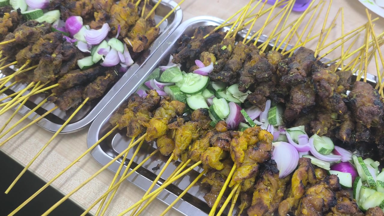 Spiedini satay di pollo e manzo appena grigliati, serviti ordinatamente all'interno di una scatola da asporto. La deliziosa carne su spiedini è disposta perfettamente su un tavolo, pronta per essere mangiata.