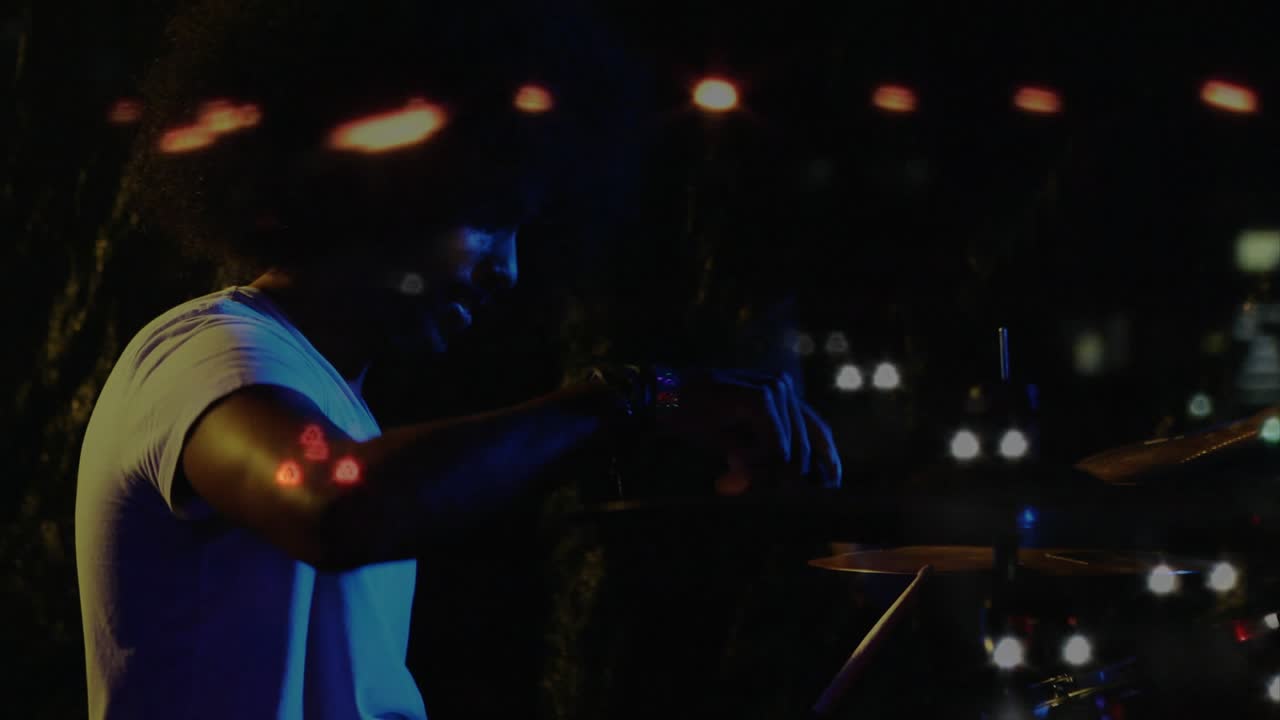 Mannlig trommeslager løfter stikker og starter jevne slag på settet, blå bokeh reagerer, drivende musikk