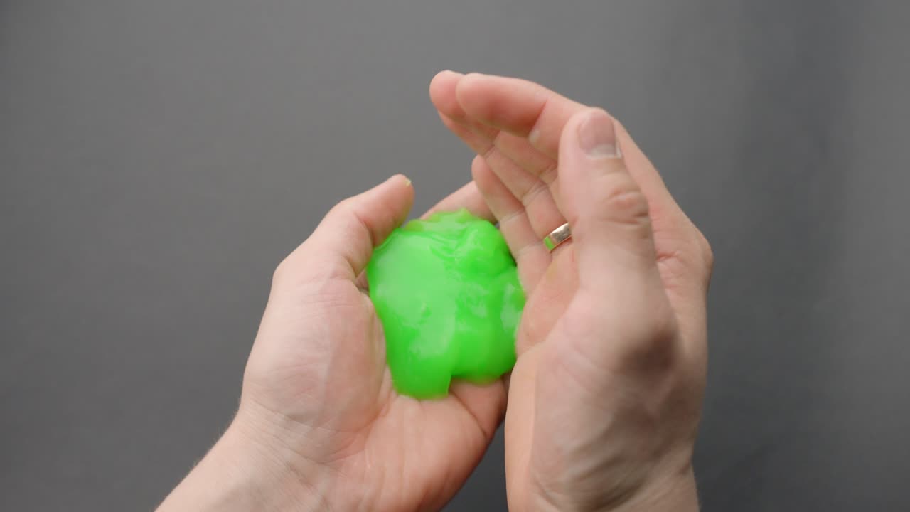 A pair of hands manipulates ultra-sticky, soft green slime that stretches easily and clings to fingers during a sensory ASMR moment, highly malleable and gooey, static camera, slow motion, close-up