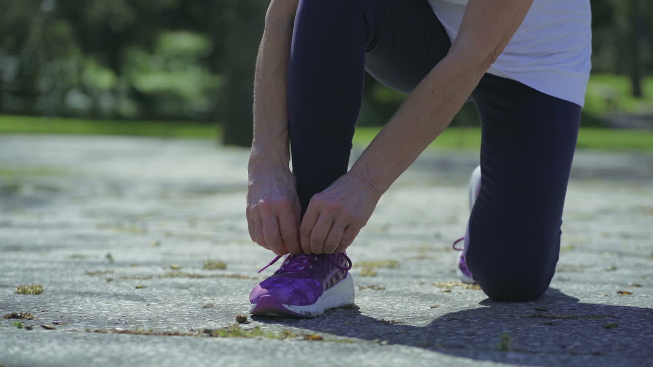 Gambe e mani giovani di donna che sistemano e allacciano i lacci delle scarpe da corsa.