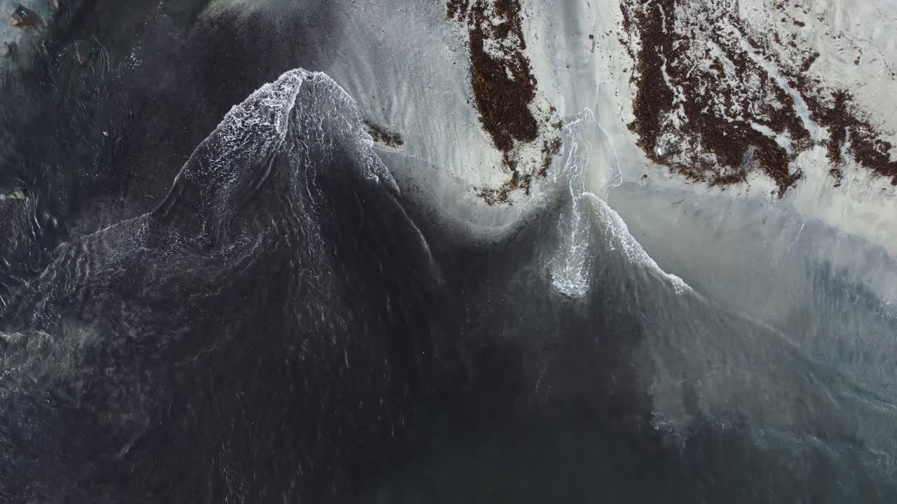 Aerial view of beautiful beach with waves and water crashing on to sandy shore from top angle