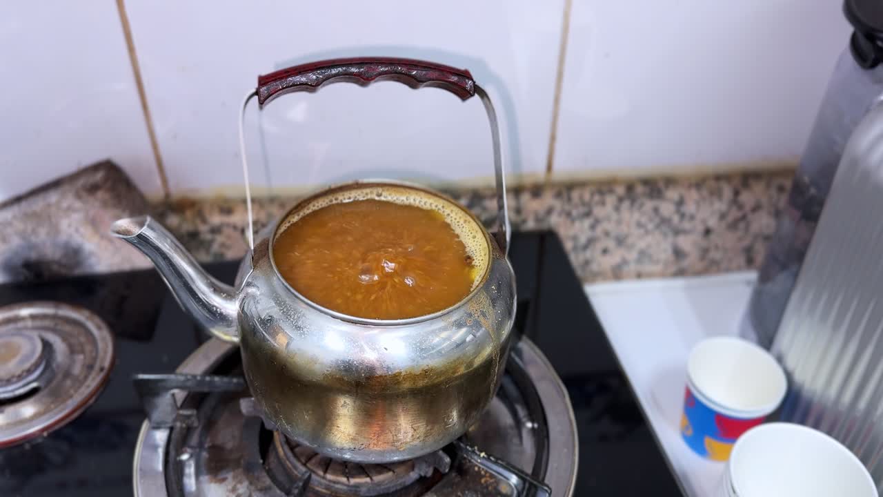 4K close up of Arabic coffee boiling in a metal pot on a gas stove showing traditional brewing and warm kitchen ambience