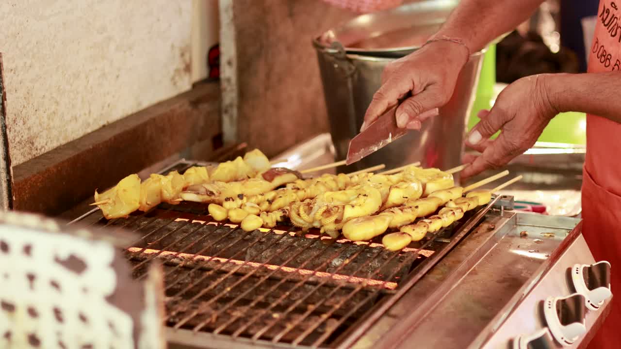 Hands grill satay skewers over open flame at Khlong Lat Mayom Floating Market, Bangkok. Warm lighting enhances the vibrant street food scene
